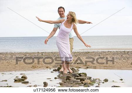 Couple at the beach walking on stones and smiling View Large Photo Image Stock Photograph - Couple at the beach walking on stones and smiling. Fotosearch