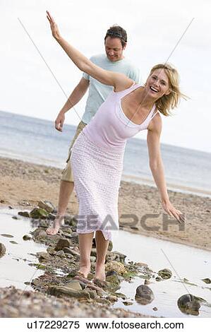 Couple at the beach walking on stones and smiling View Large Photo Image Stock Photography - Couple at the beach walking on stones and smiling. Fotosearch