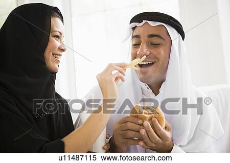 Stock Photography - Couple eating fast food in living room and smiling (high key/selective focus). Fotosearch