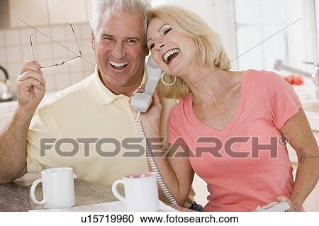 Stock Image - Couple in kitchen using telephone together and laughing. Fotosearch