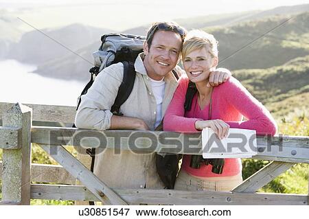 Stock Photo - Couple on cliffside outdoors leaning on railing and smiling. Fotosearch