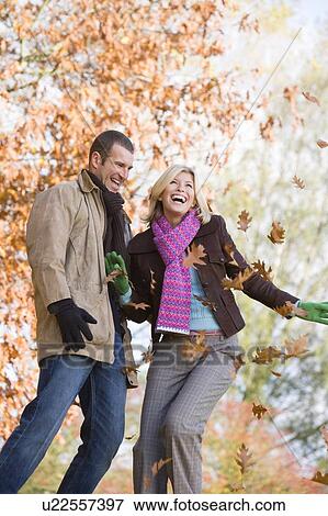 Stock Photo - Couple outdoors playing in leaves and smiling (selective focus). Fotosearch