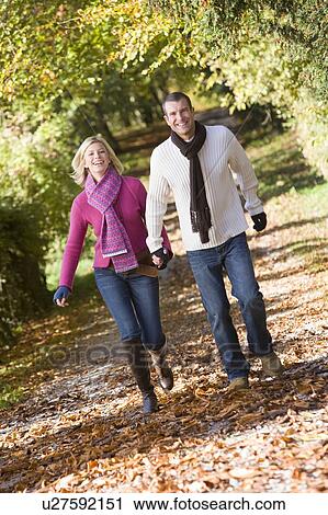 Couple outdoors running on path in park holding hands smiling (selective focus) View Large Photo Image Stock Image - Couple outdoors running on path in park holding hands smiling (selective focus). Fotosearch