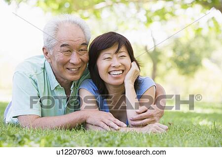 Stock Image - Couple relaxing outdoors in park smiling. Fotosearch