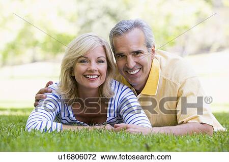 Stock Image - Couple relaxing outdoors in park smiling. Fotosearch