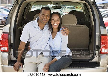 Stock Image - Couple sitting in back of van smiling. Fotosearch