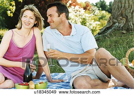 Couple sitting outdoors with picnic smiling View Large Photo Image Stock Photo - Couple sitting outdoors with picnic smiling. Fotosearch