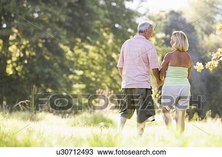 Stock Image - Couple walking in park holding hands. Fotosearch