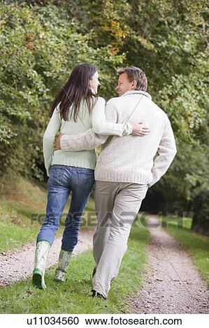 Stock Image - Couple walking outdoors on path in park smiling (selective focus). Fotosearch