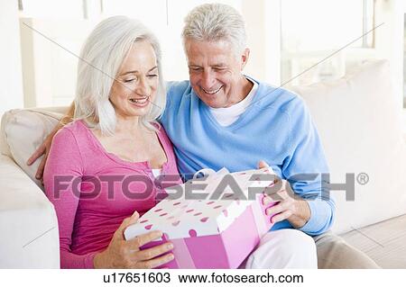 Stock Image - Husband giving wife gift in living room smiling. Fotosearch