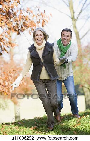 Stock Image - Senior couple outdoors running around and smiling (selective focus). Fotosearch