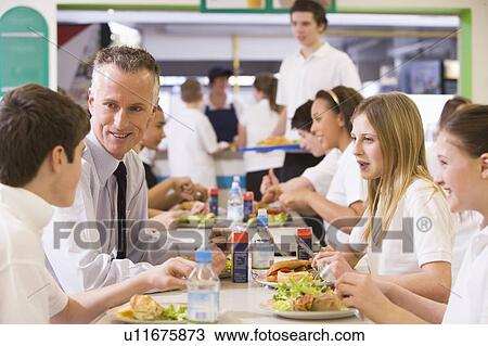 Stock Image - Students and teacher having lunch in dining hall. Fotosearch