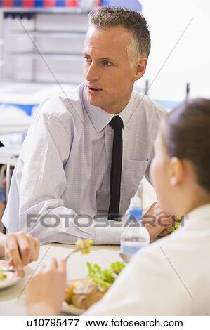 Stock Photo - Students and teacher having lunch in dining hall. Fotosearch