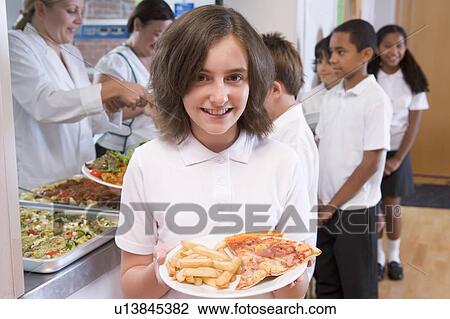 Stock Image - Students in cafeteria line with one holding unhealthy meal looking at camera (depth of field). Fotosearch