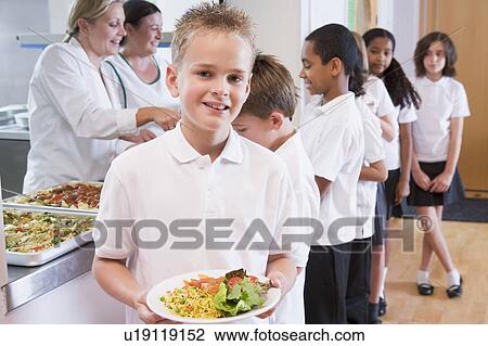 Stock Image - Students in cafeteria line with one holding his healthy meal and looking at camera (depth of field). Fotosearch