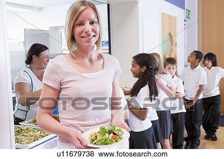 Stock Photo - Students in cafeteria line with teacher holding her healthy meal and looking at camera (depth of field). Fotosearch