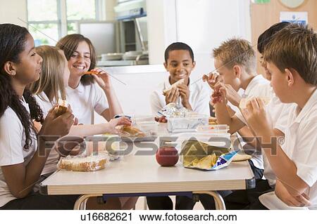 Stock Image - Students sitting at cafeteria table eating lunch (depth of field). Fotosearch