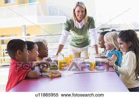 Teacher leaning on table outdoors while students eat lunch (high key) View Large Photo Image Stock Photography - Teacher leaning on table outdoors while students eat lunch (high key). Fotosearch