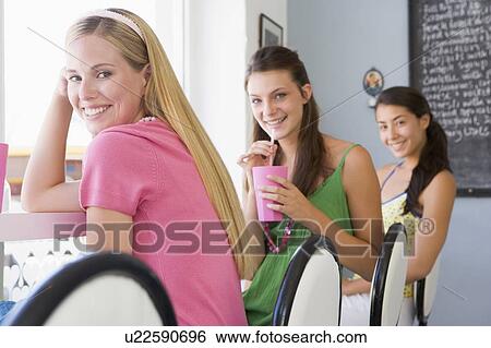 Three young women having a cold drink in a cafeteria View Large Photo Image Stock Photograph - Three young women having a cold drink in a cafeteria. Fotosearch