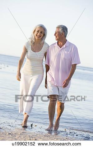 Stock Image - Couple at the beach holding hands and smiling. Fotosearch