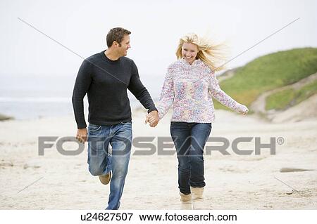 Couple running at beach holding hands smiling View Large Photo Image Stock Photo - Couple running at beach holding hands smiling. Fotosearch