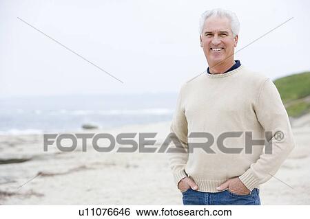 Stock Photograph - Man at the beach with hands in pockets smiling. Fotosearch
