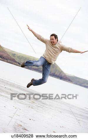 Stock Photo - Man jumping on beach smiling. Fotosearch