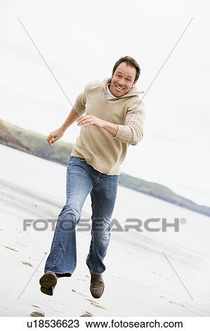 Stock Image - Man running on beach smiling. Fotosearch