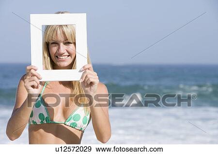 Stock Photo - Woman on a beach holding a frame to her face. Fotosearch