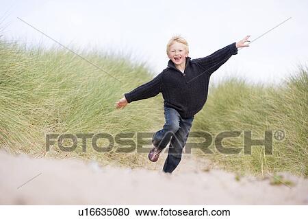 Stock Image - Young boy running on beach smiling. Fotosearch