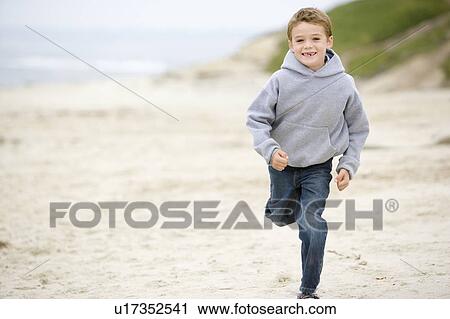 Stock Image - Young boy running on beach smiling. Fotosearch