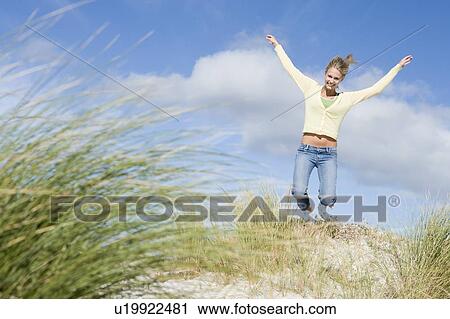 Stock Image - Young woman jumping on a sand hill. Fotosearch