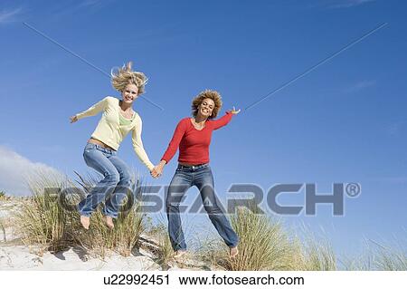 Stock Image - Young woman jumping on a sand hill. Fotosearch