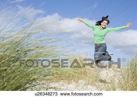 Stock Image - Young woman jumping on a sand hill. Fotosearch