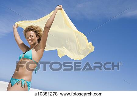 Stock Photo - Young woman posing with a scarf on a beach. Fotosearch
