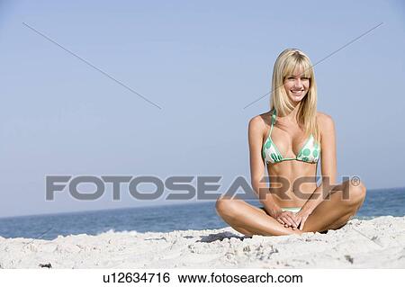 Stock Photograph - Young woman sitting on a beach. Fotosearch