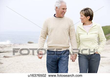 Stock Image - Couple at the beach holding hands and smiling. Fotosearch