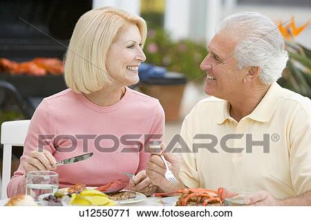 Stock Image - Couple Enjoying A Barbequed Meal In The Garden. Fotosearch