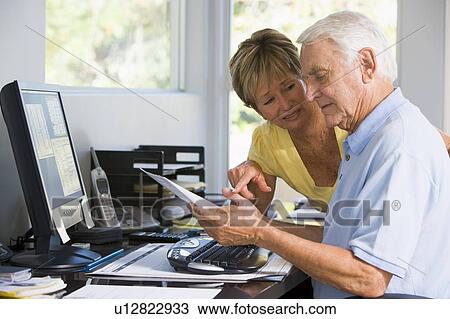 Stock Image - Couple in home office with computer and paperwork. Fotosearch