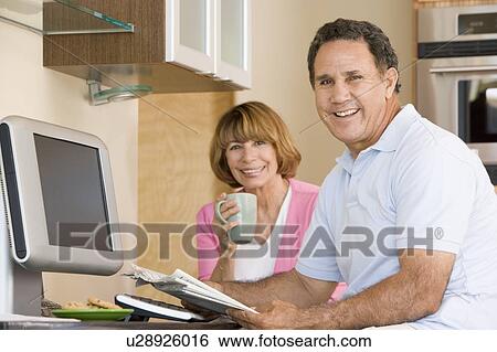 Stock Photograph - Couple in kitchen with coffee and newspaper smiling. Fotosearch