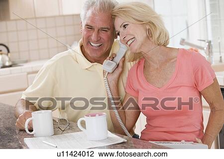 Stock Image - Couple in kitchen with coffee using telephone together and smiling. Fotosearch