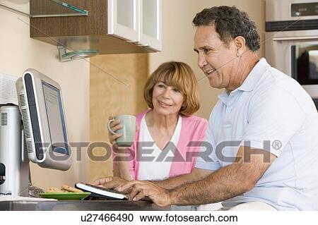 Stock Image - Couple in kitchen with computer and coffee smiling. Fotosearch