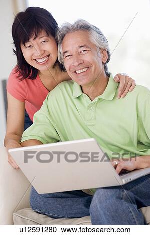Stock Image - Couple in living room with laptop smiling. Fotosearch