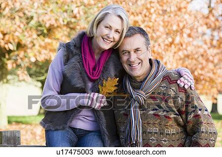 Couple outdoors in park by fence smiling (selective focus) View Large Photo Image Stock Image - Couple outdoors in park by fence smiling (selective focus). Fotosearch