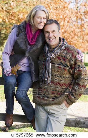 Couple outdoors in park by fence smiling (selective focus) View Large Photo Image Stock Photography - Couple outdoors in park by fence smiling (selective focus). Fotosearch