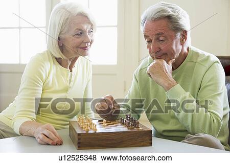 Stock Photo - Couple playing chess in living room smiling. Fotosearch