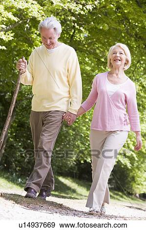 Couple walking on path in park holding hands and smiling View Large Photo Image Stock Photo - Couple walking on path in park holding hands and smiling. Fotosearch