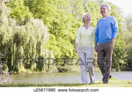 Stock Image - Couple walking outdoors at park by lake smiling. Fotosearch
