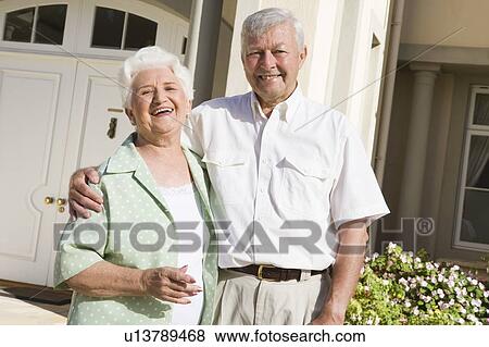 Stock Photo - Senior couple standing outside their home. Fotosearch