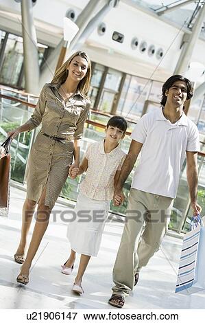 Stock Photo - Family walking in mall holding hands and smiling (selective focus). Fotosearch